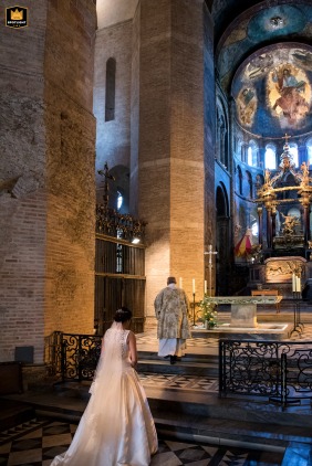During the religious ceremony inside the Basilique St-Sernin in Toulouse, the bride and the priest walk together toward the altar to sign the official marriage register.